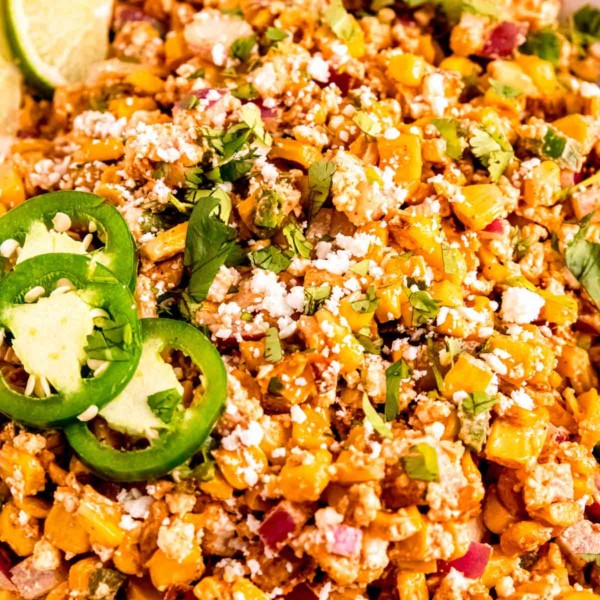 very close up image of Mexican street corn in white bowl topped with jalapenos