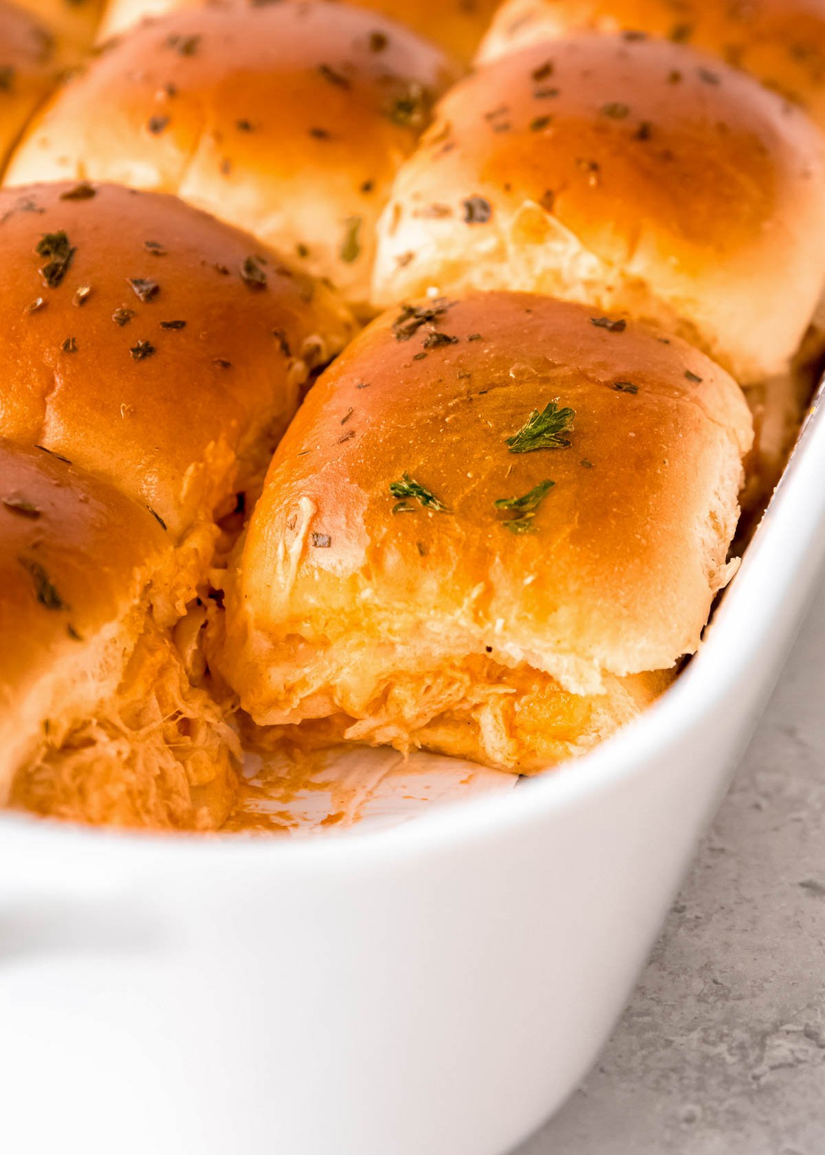 a baking dish full of baked buffalo chicken sliders, sprinkled with herbs