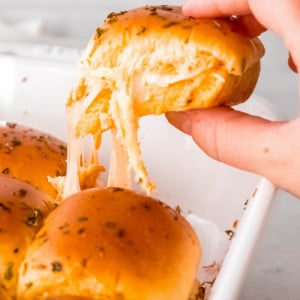 a hand grabbing a buffalo chicken slider from a casserole dish; gooey, melted cheese strings down