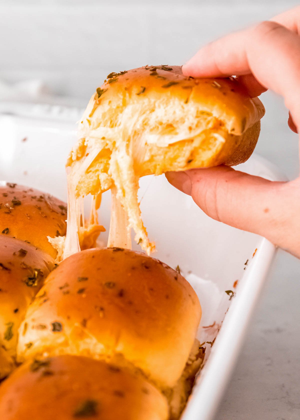 a hand grabbing a buffalo chicken slider from a casserole dish; gooey, melted cheese strings down