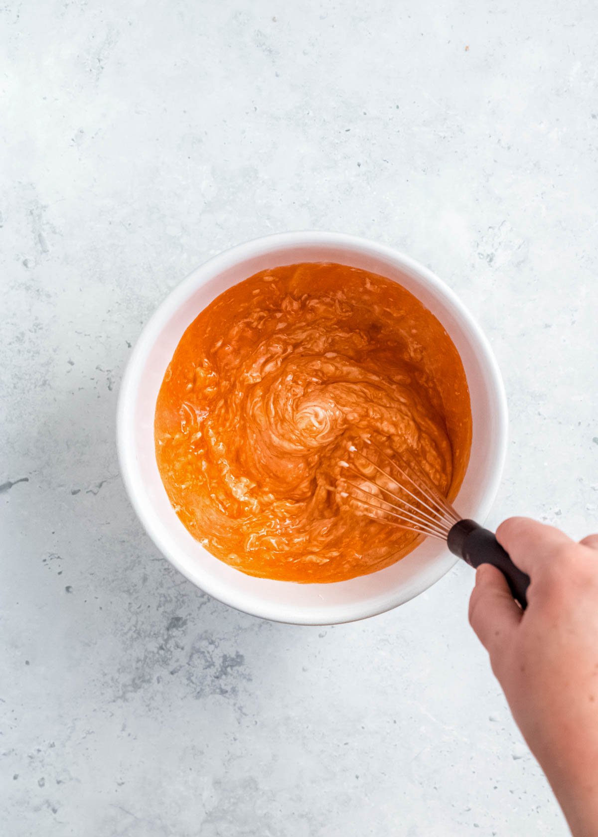 buffalo sauce and softened cream cheese being mixed in a white bowl