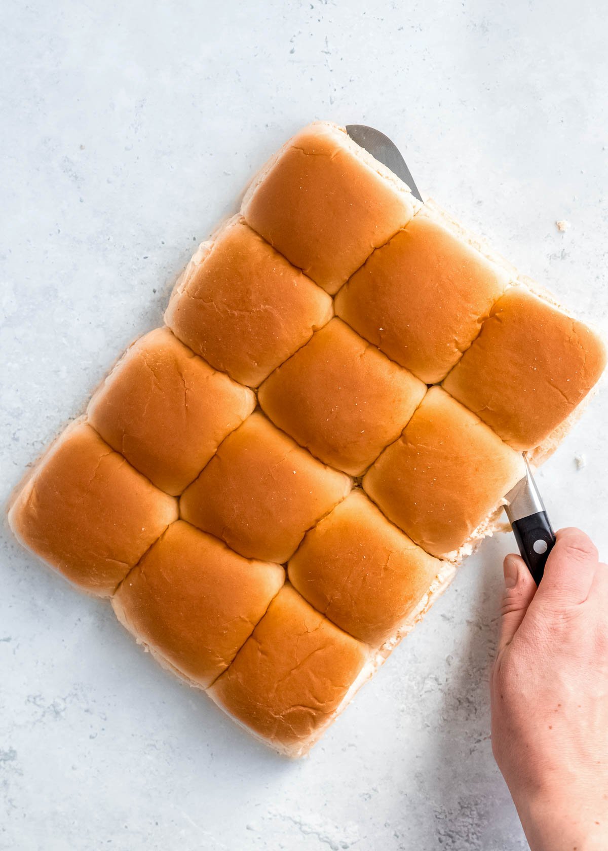 a hand using a knife to slice the buns in half, parallel to the countertop