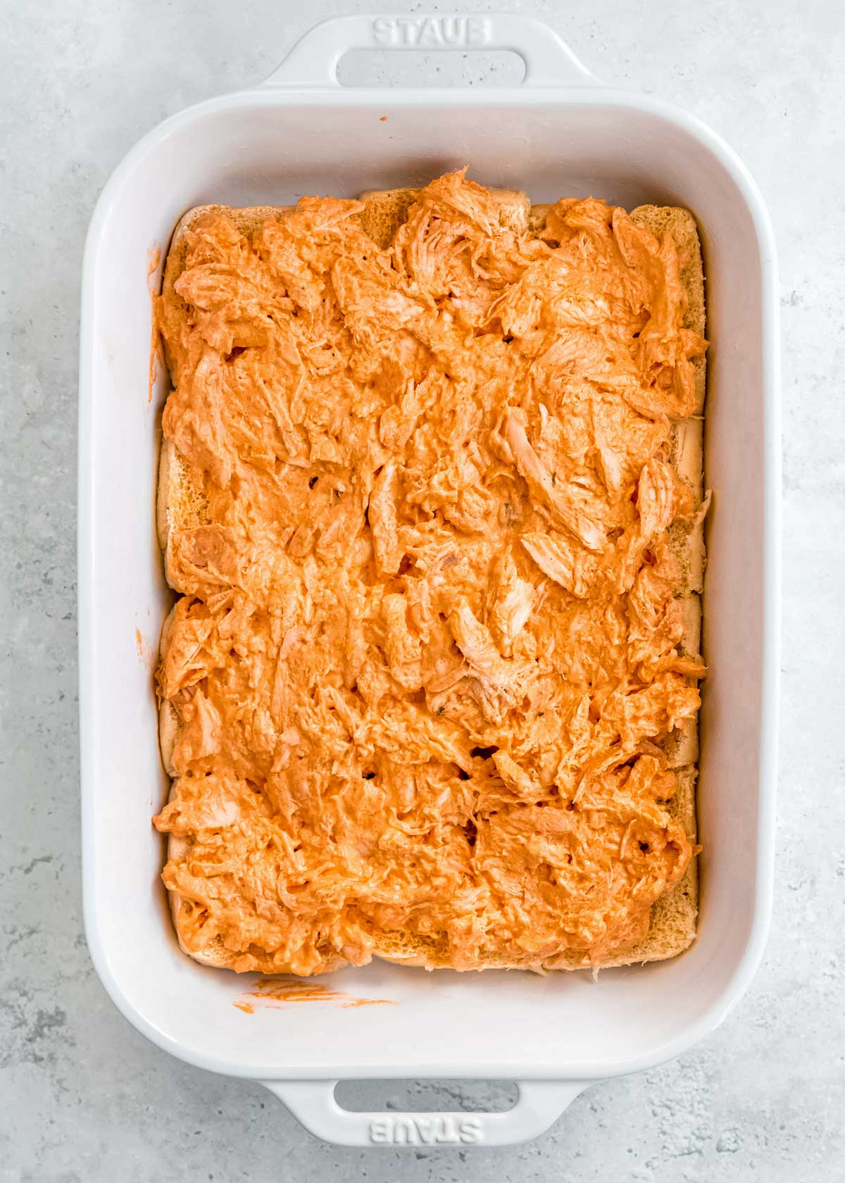 creamy buffalo chicken spread over the bottom buns in a white casserole dish