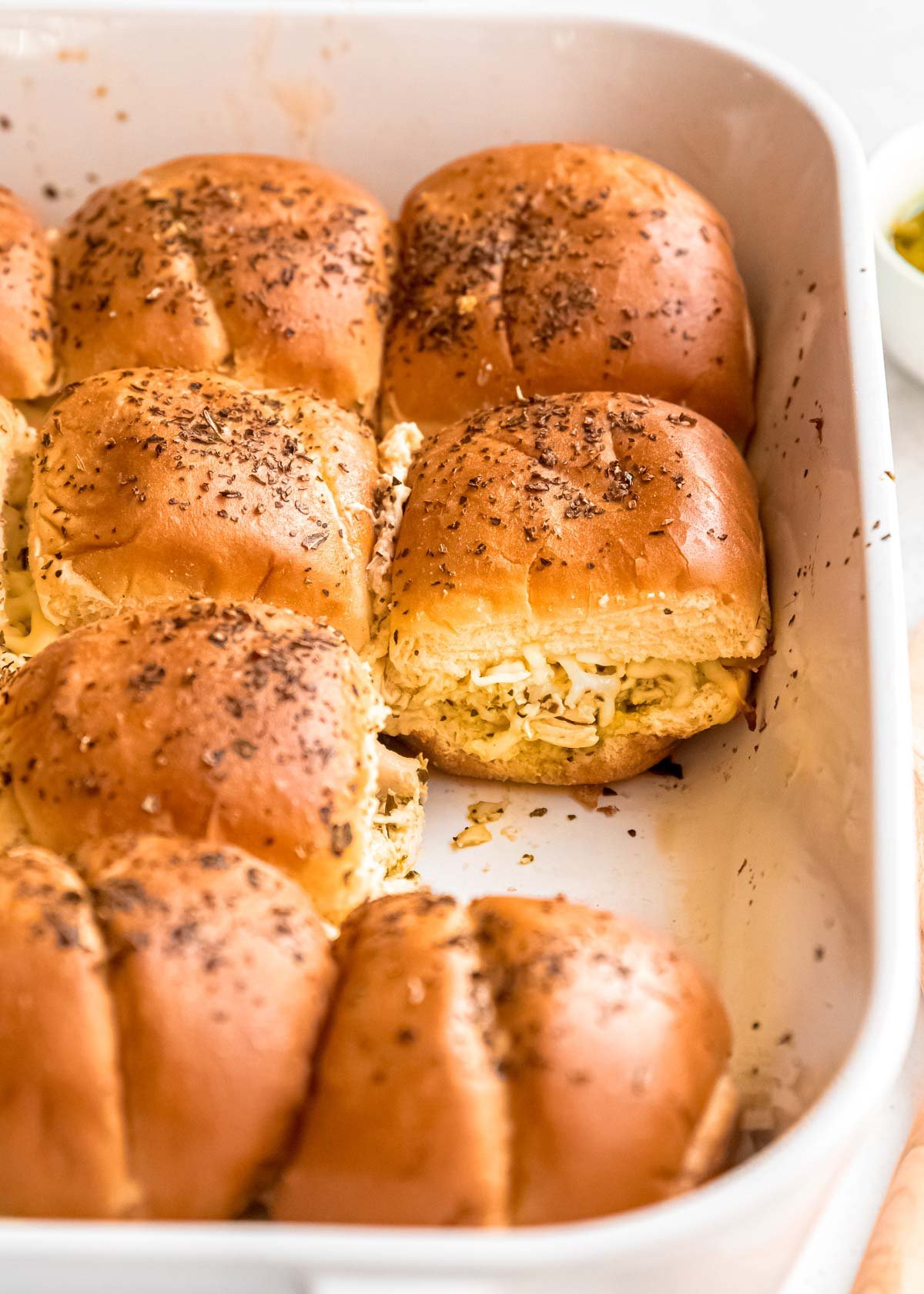 cheesy pesto chicken sliders in a white casserole dish