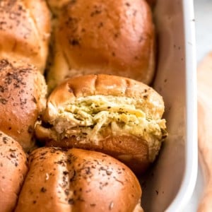 a casserole dish filled with cheesy pesto chicken sliders