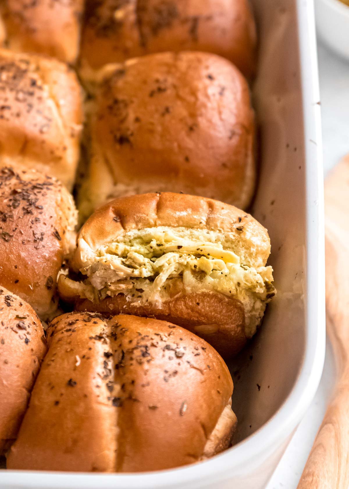 a casserole dish filled with cheesy pesto chicken sliders