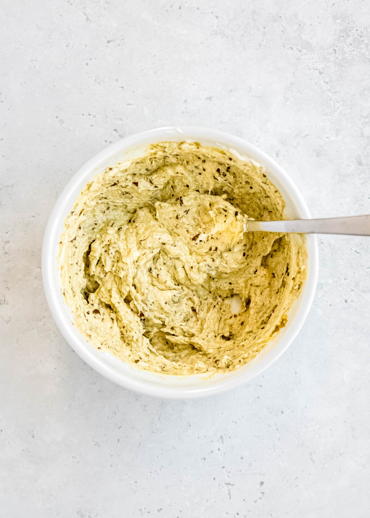 cream cheese and pesto mixing together in a white bowl