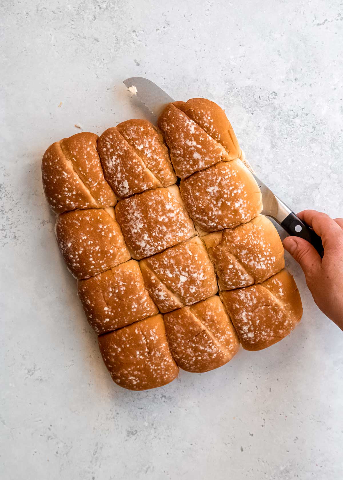 a hand using a bread knife to slice rolls in half, parallel to the countertop