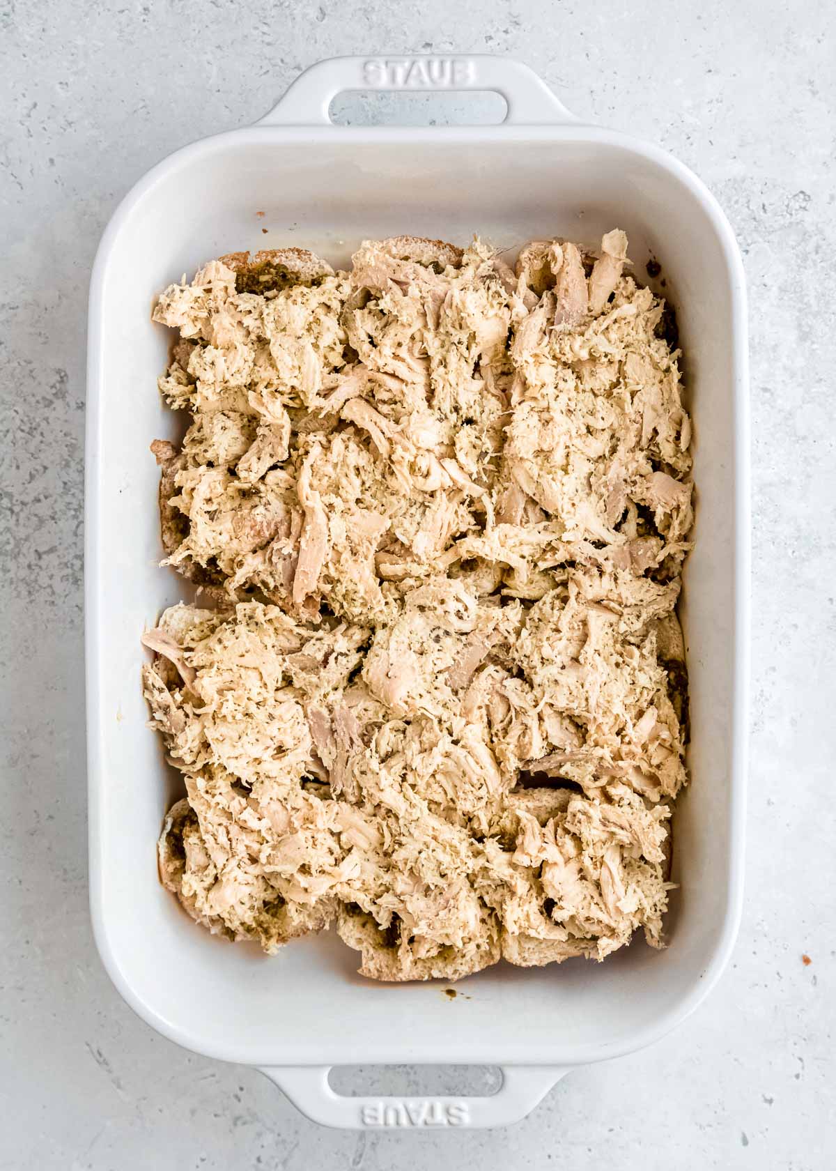 creamy chicken pesto spread over rolls in a white baking dish