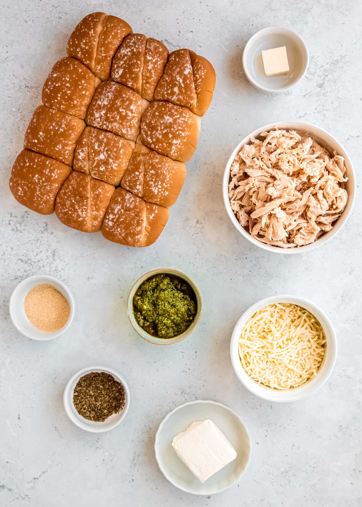 ingredients for cheesy pesto chicken sliders on a white countertop