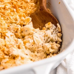 close up image of a wooden spoon scooping a bite of poppy seed chicken casserole out of baking dish