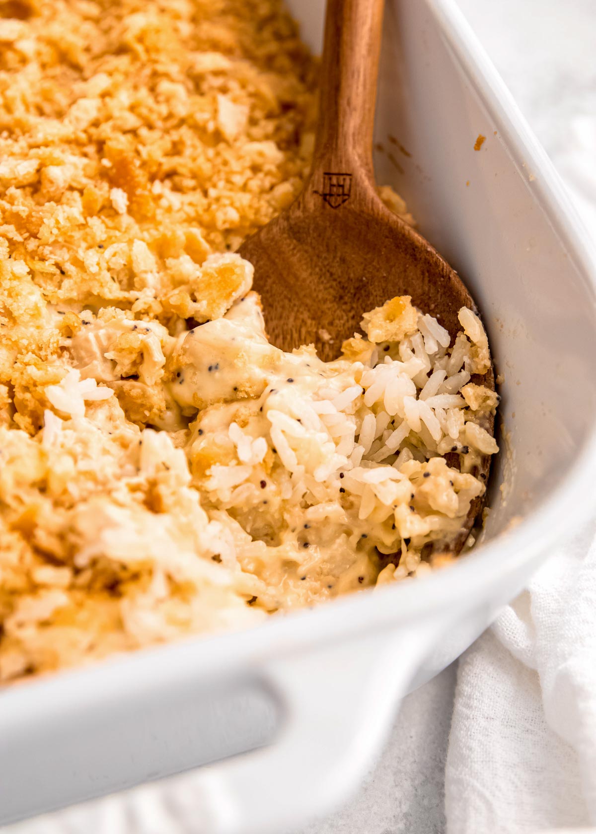 close up image of a wooden spoon scooping a bite of poppy seed chicken casserole out of baking dish