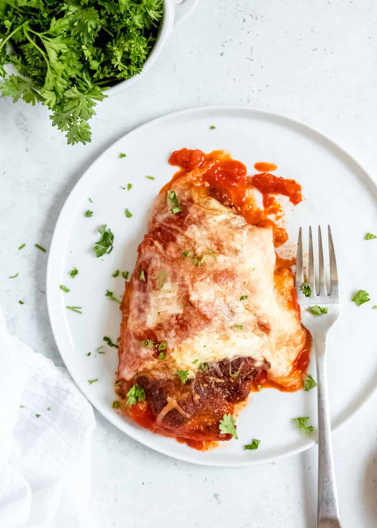 overhead image of one piece of chicken parmesan and fork on white plate