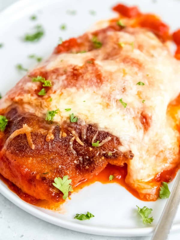 close up image of chicken parmesan on white plate