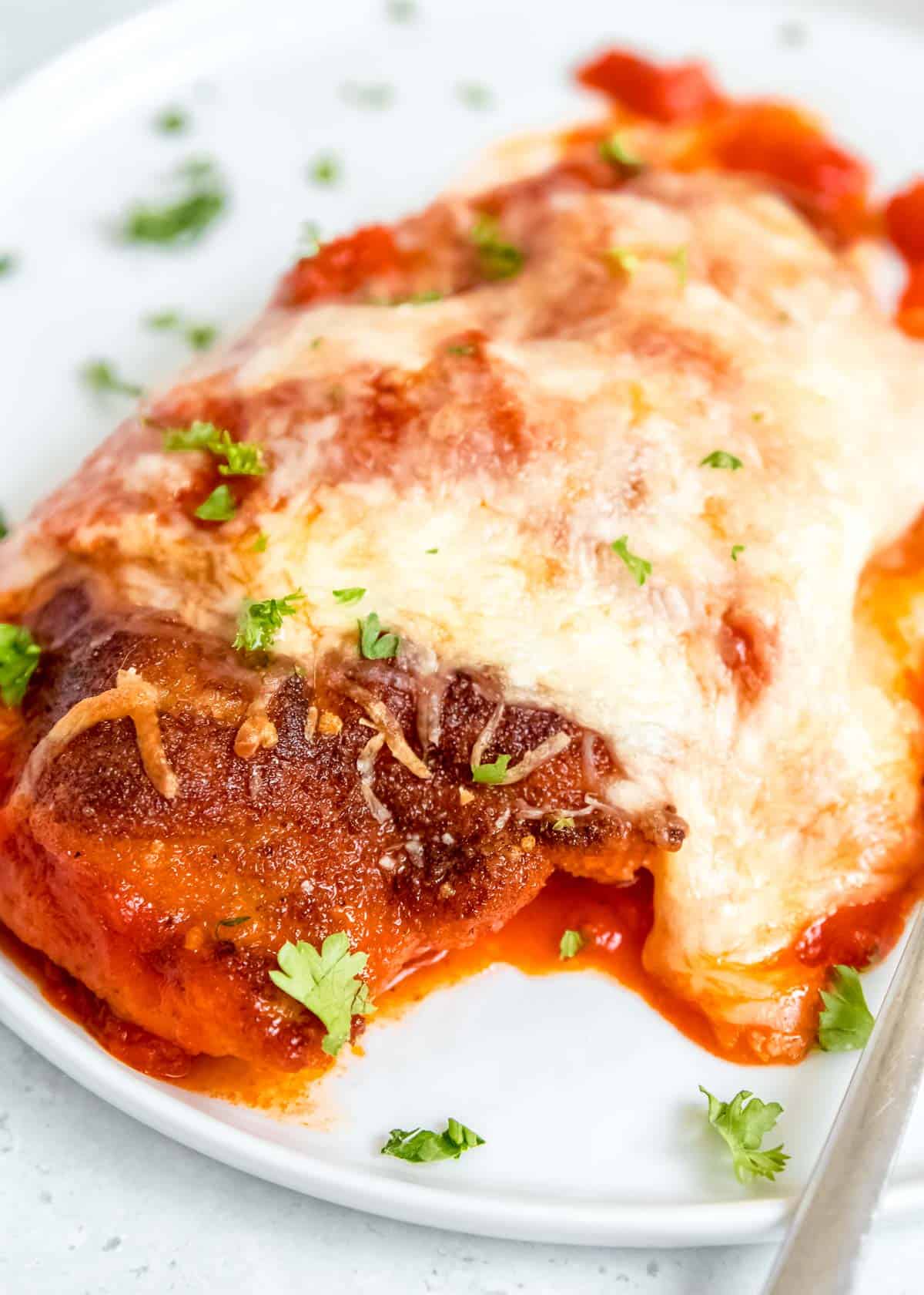 close up image of chicken parmesan on white plate