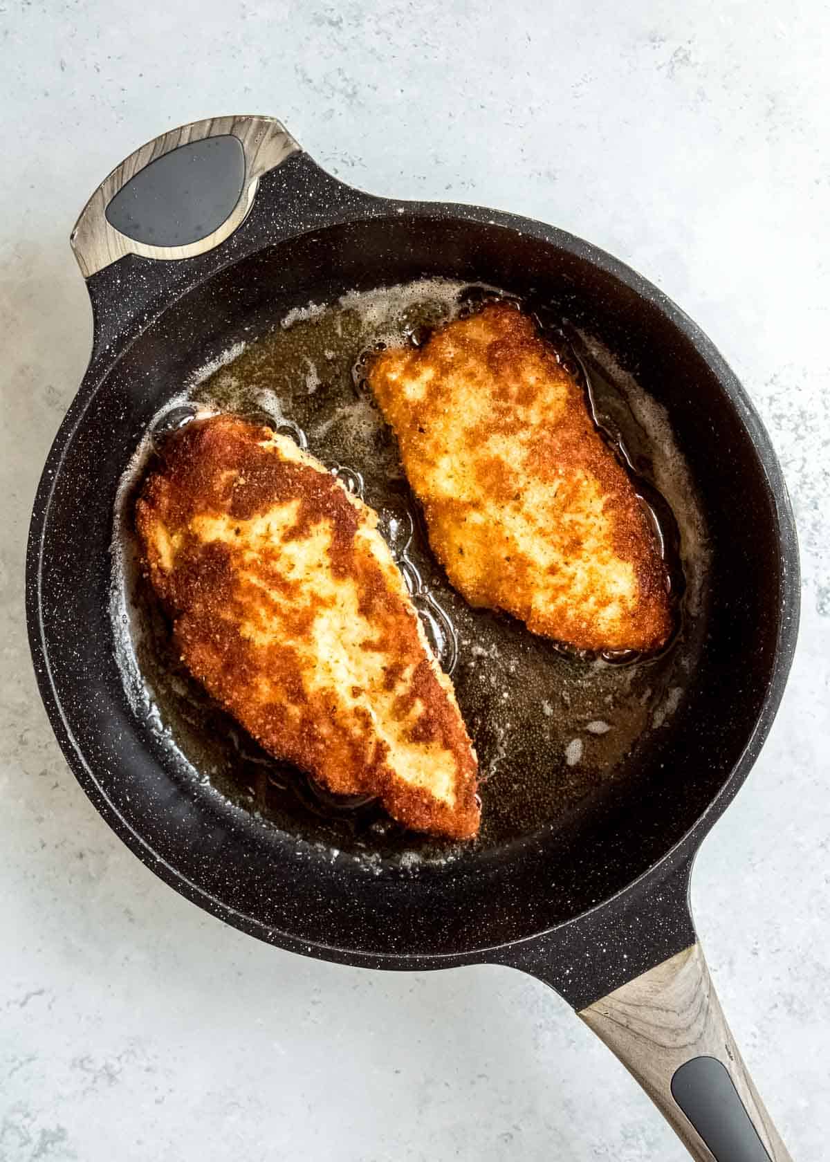 chicken being fried in cast iron skillet