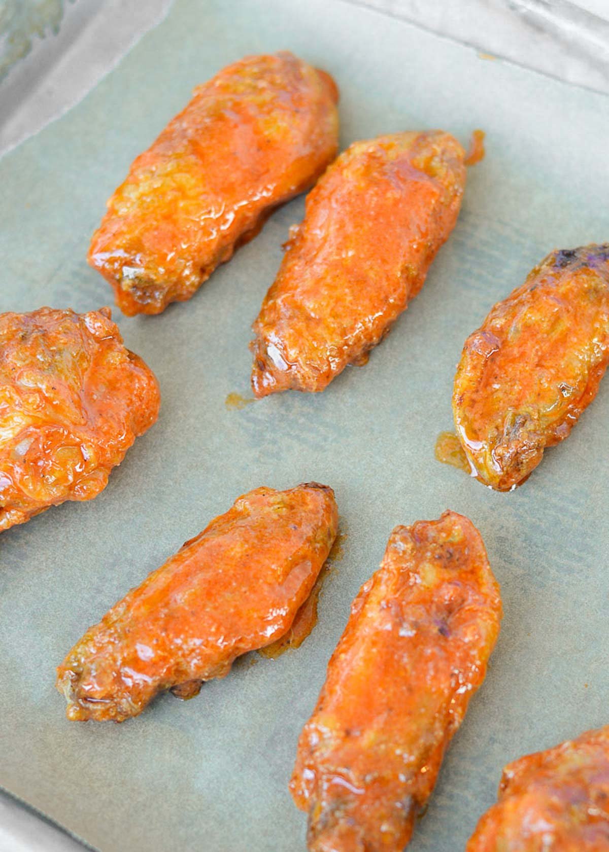 saucy air fryer chicken wings coated in buffalo sauce on parchment paper