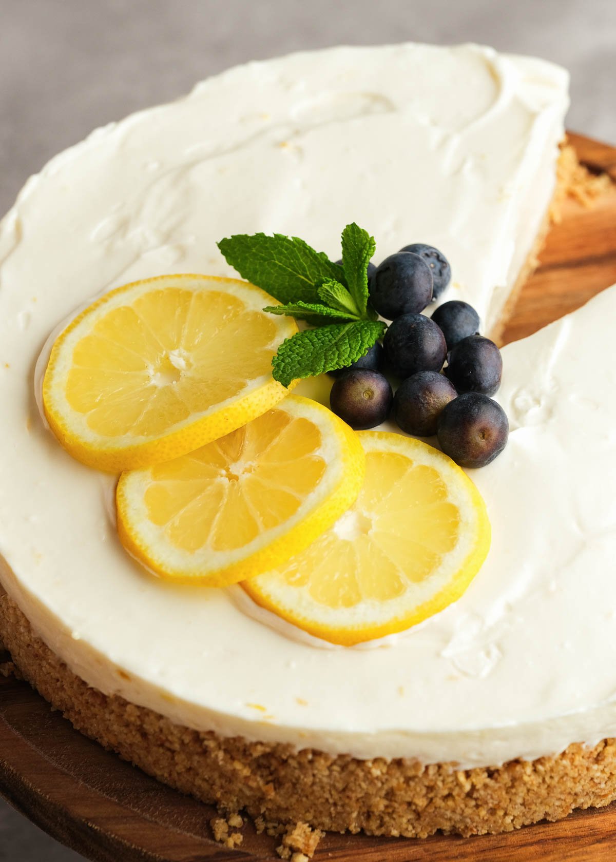 lemon slices, mint leaves, and fresh blueberries atop a creamy lemon cheesecake with a graham cracker crust