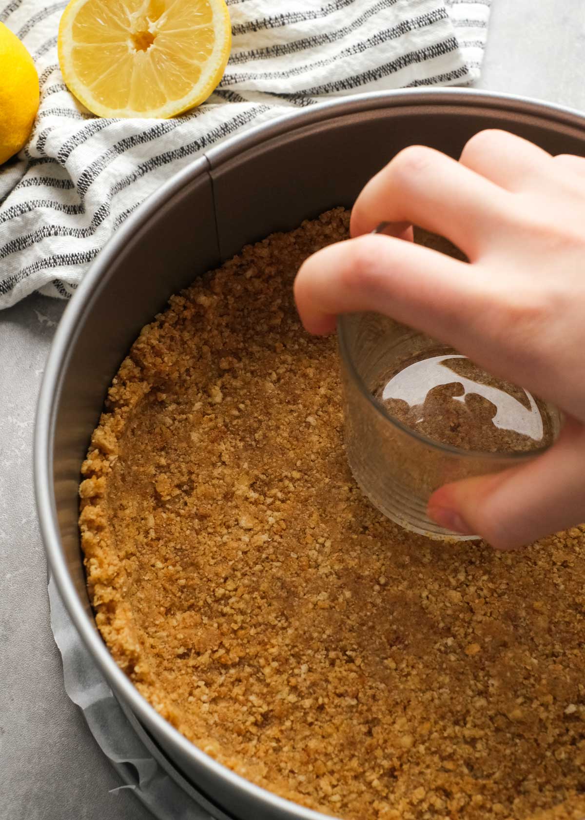 cheesecake crust being pressed into a springform pan with a glass