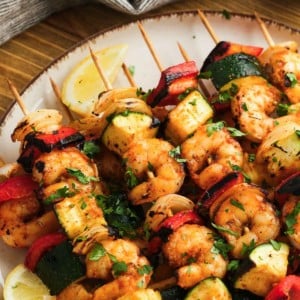 a plate loaded with many shrimp and vegetable kabobs with lemon wedges on the side