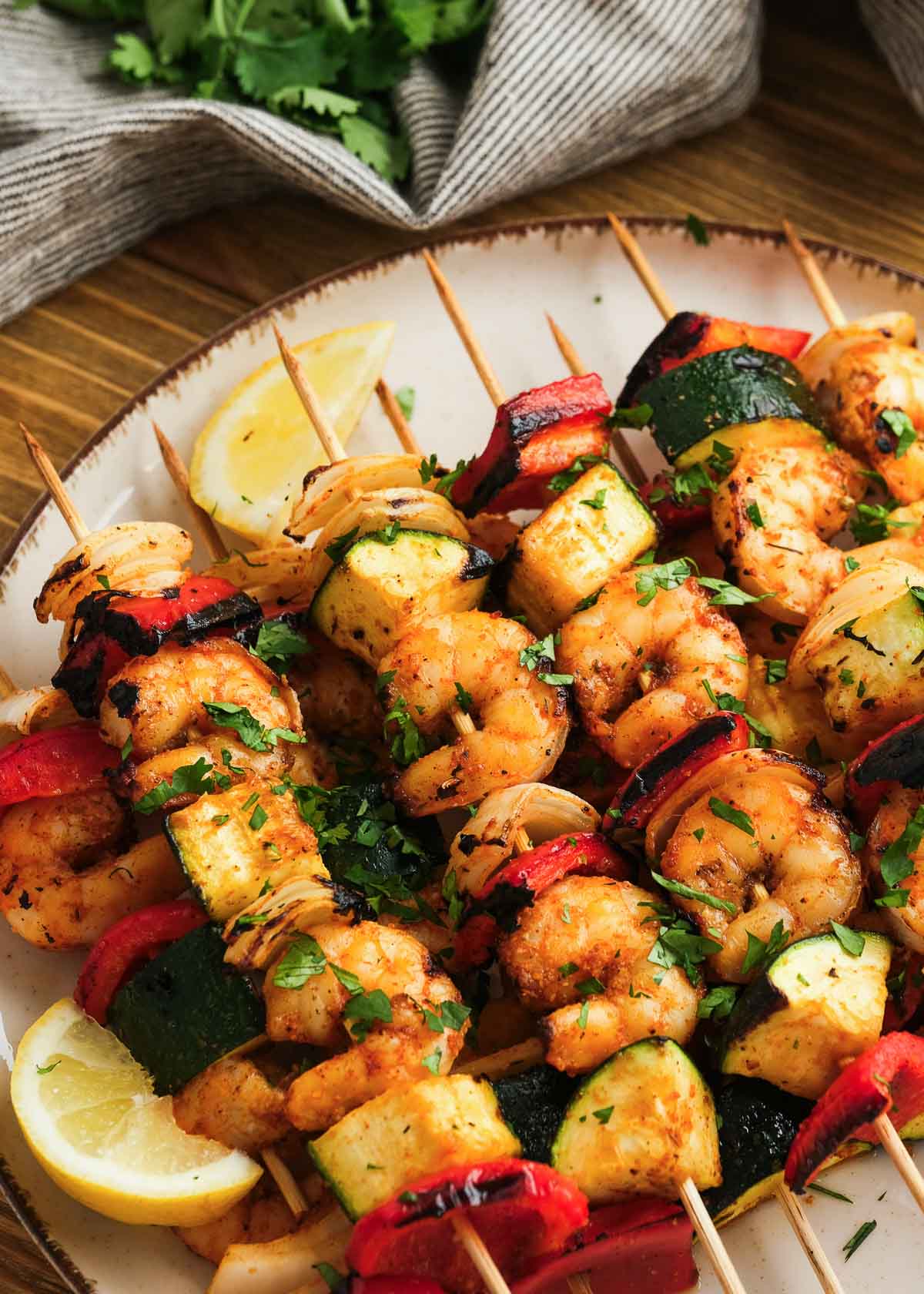 a plate loaded with many shrimp and vegetable kabobs with lemon wedges on the side
