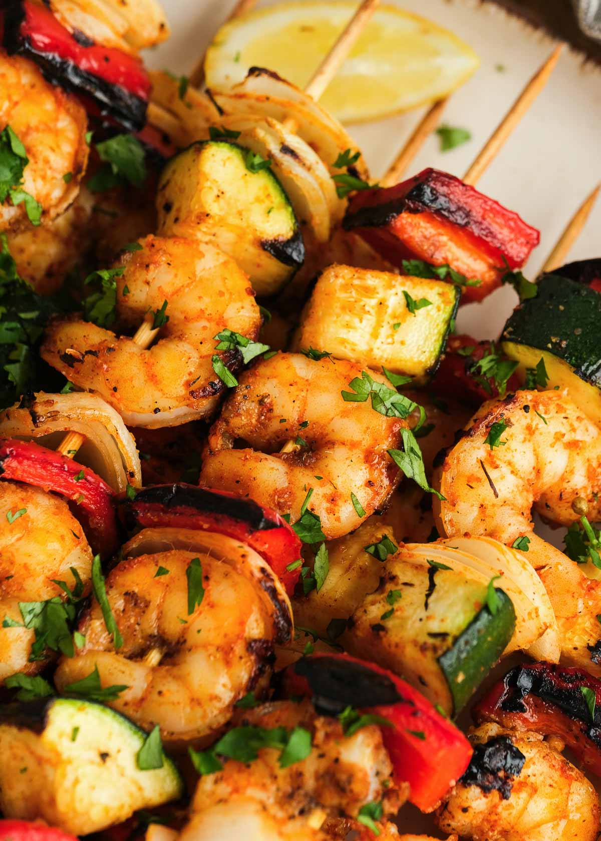 closeup view of several shrimp and vegetable kabobs on a plate with lemon wedges