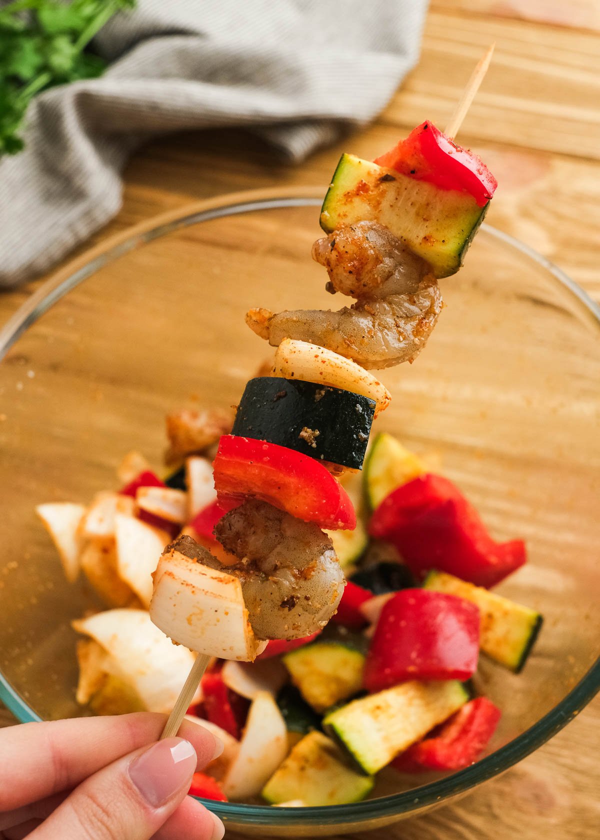 pieces of red bell pepper, zucchini, shrimp, and onion being pierced by a skewer