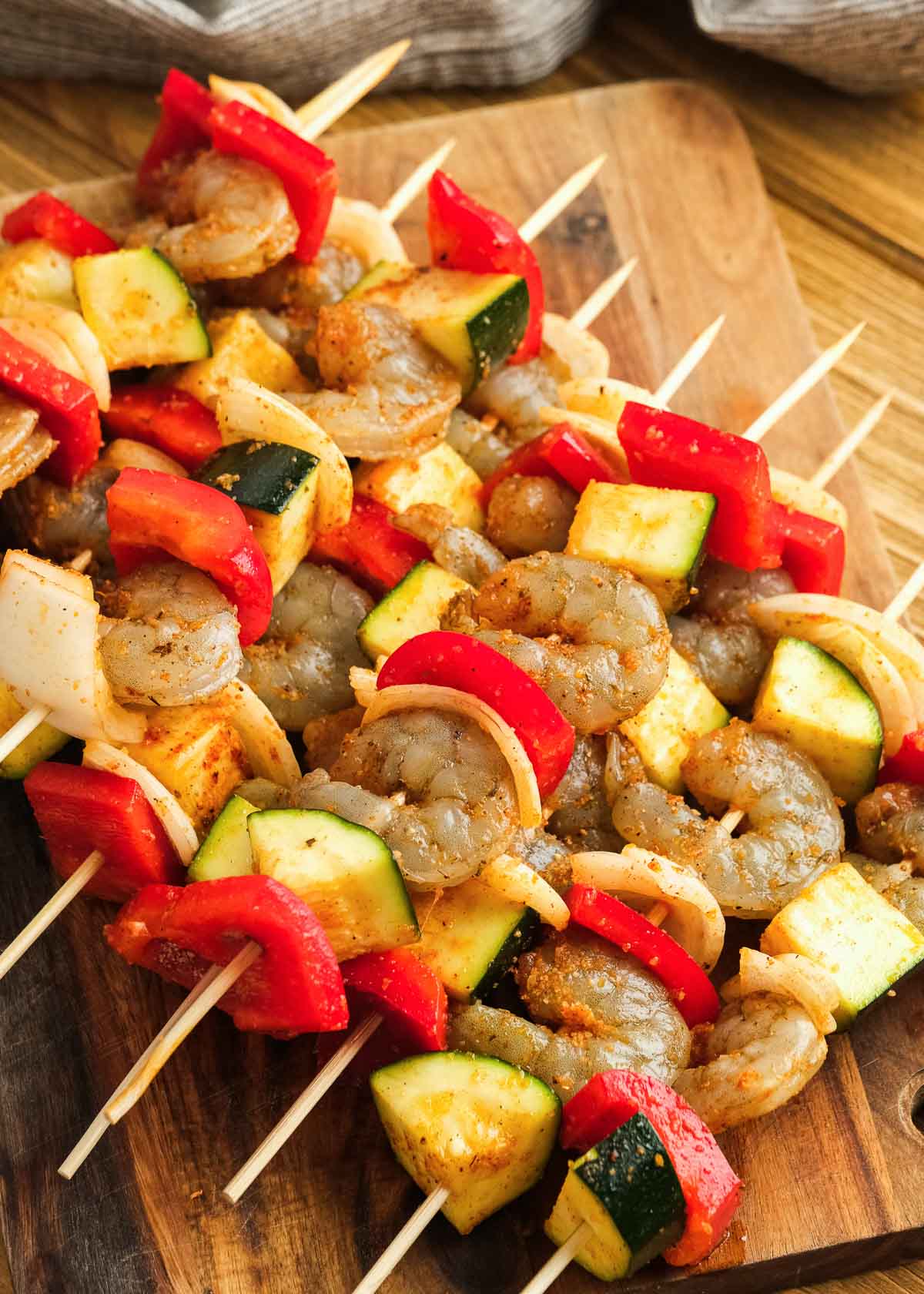 several raw shrimp kabobs assembled on a wooden cutting board, alternating between veggies and shrimp
