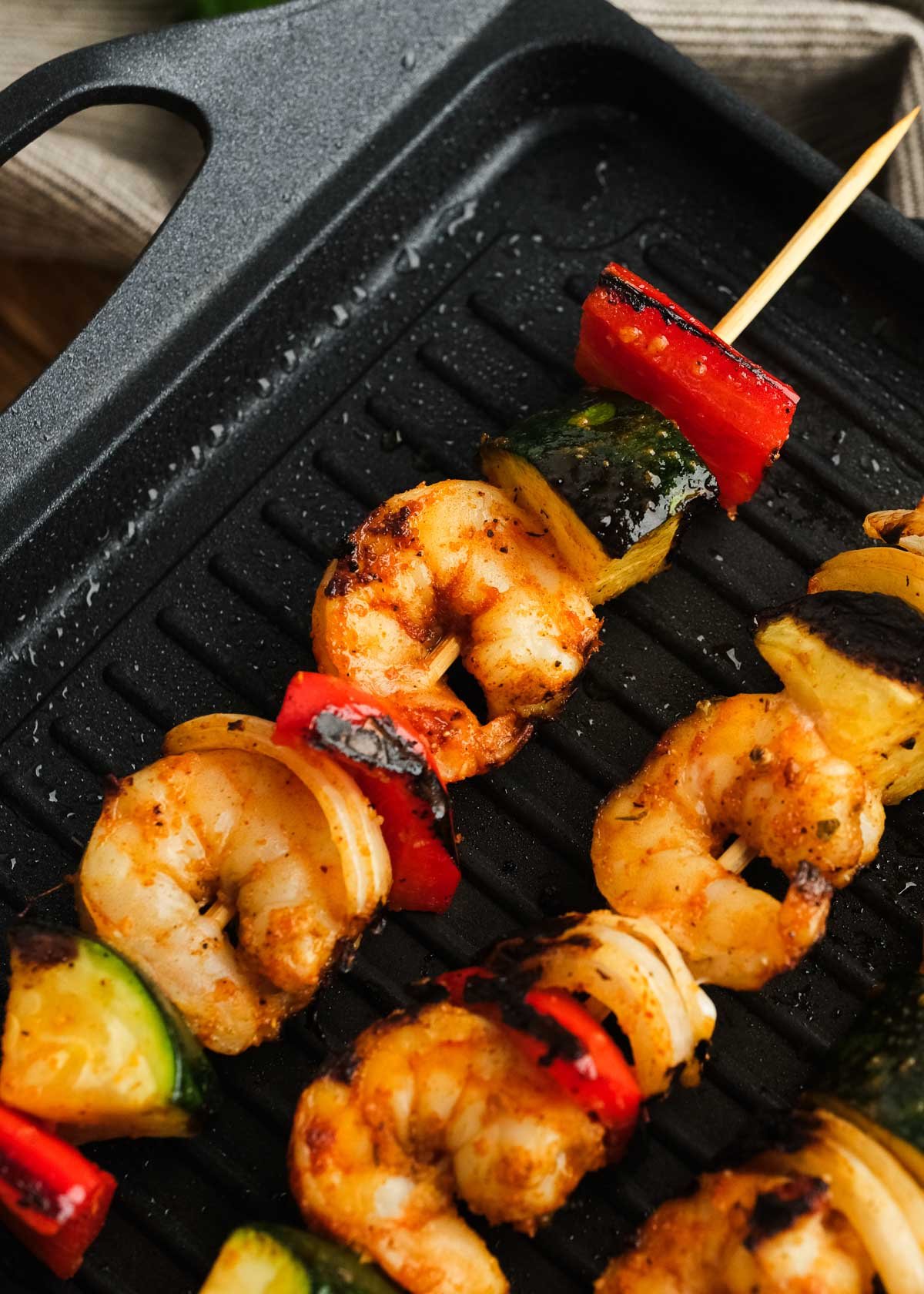 juicy shrimp, bell peppers, onion, and zucchini assembled on a skewer and cooking on the grill