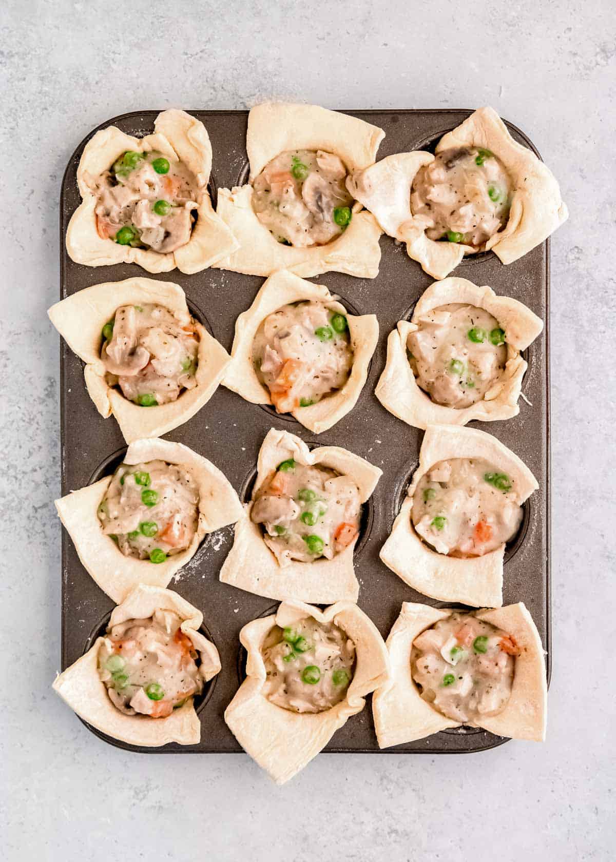 creamy chicken and veggie filling in puff pastry cups in a muffin pan