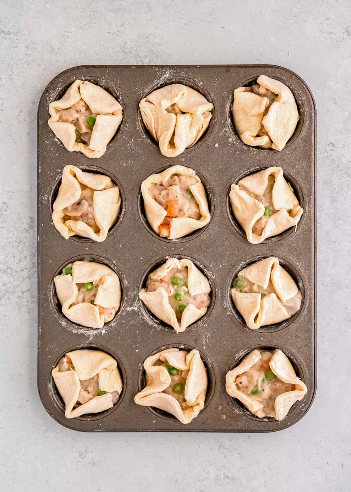 puff pastry corners folded in to form mini chicken pot pies in a muffin pan