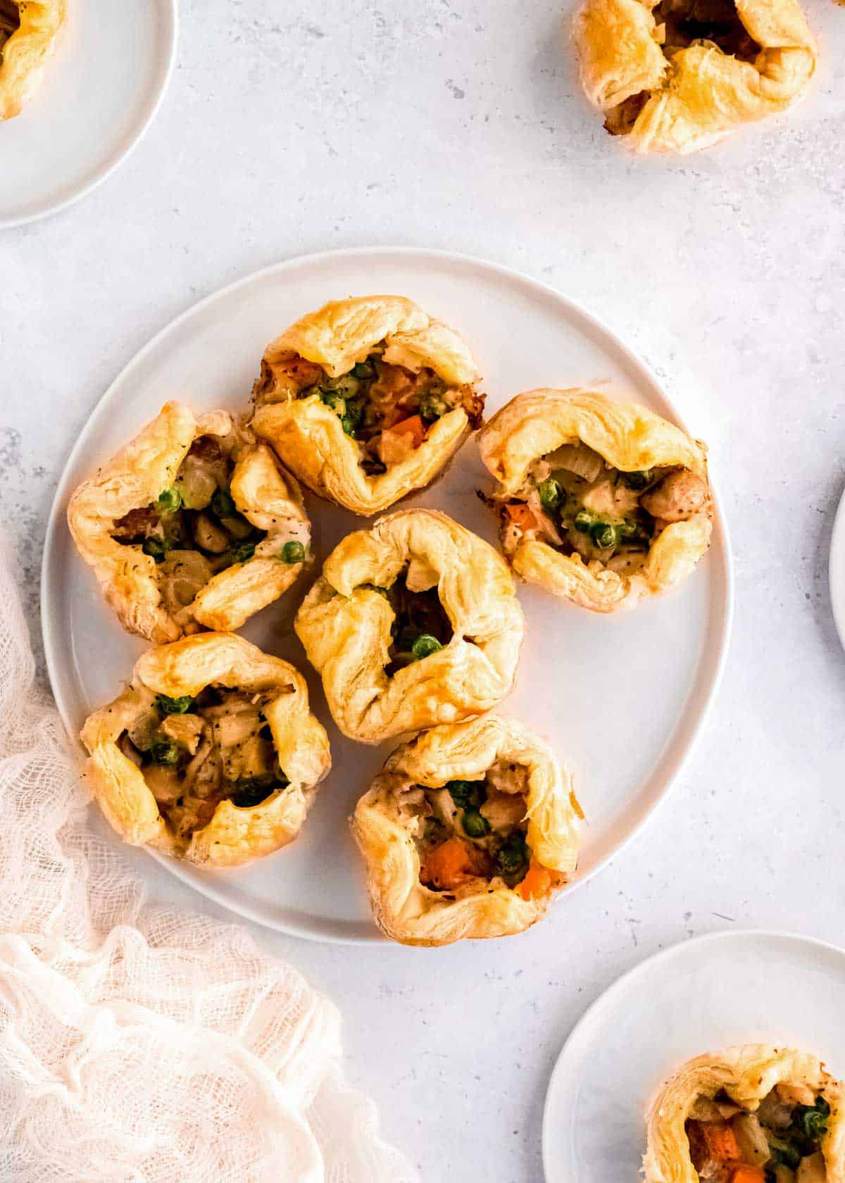 six mini chicken pot pies on a platter in the center of a table surrounded by small plates with puff pastry pot pies