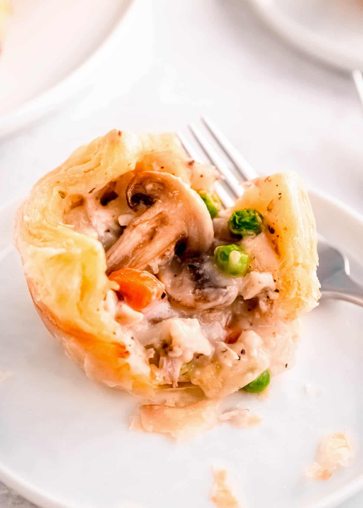 a fork beside a puff pastry pot pie, showing the mushrooms, peas, carrots, and chicken inside