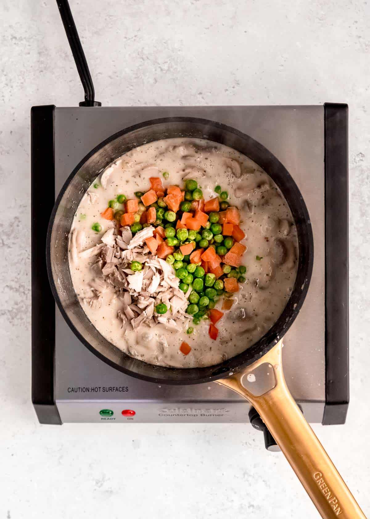 peas, carrots, and chicken in a pot with a creamy vegetable pot pie filling