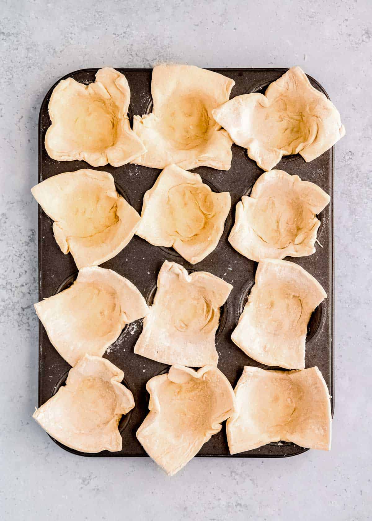 a 12-count muffin pan filled with puff pastry rectangles to form cups