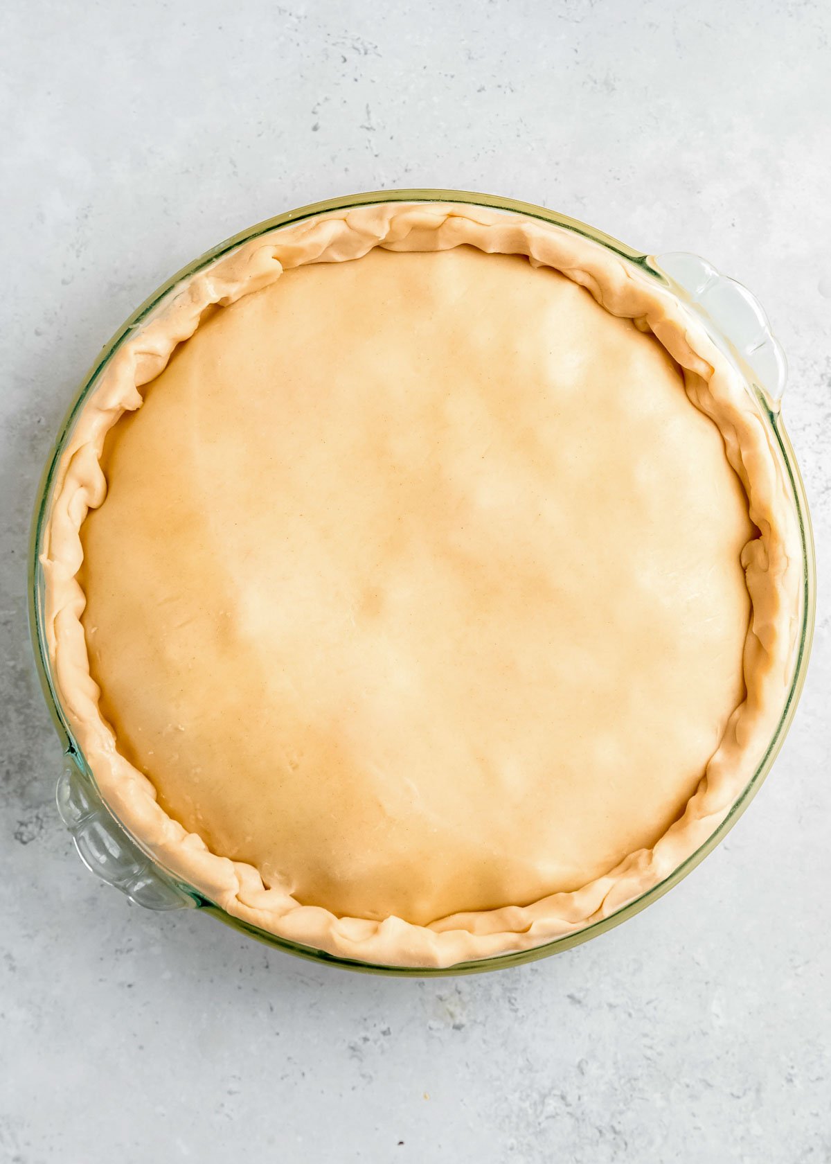 overhead image of second pie crust being added to pot pie