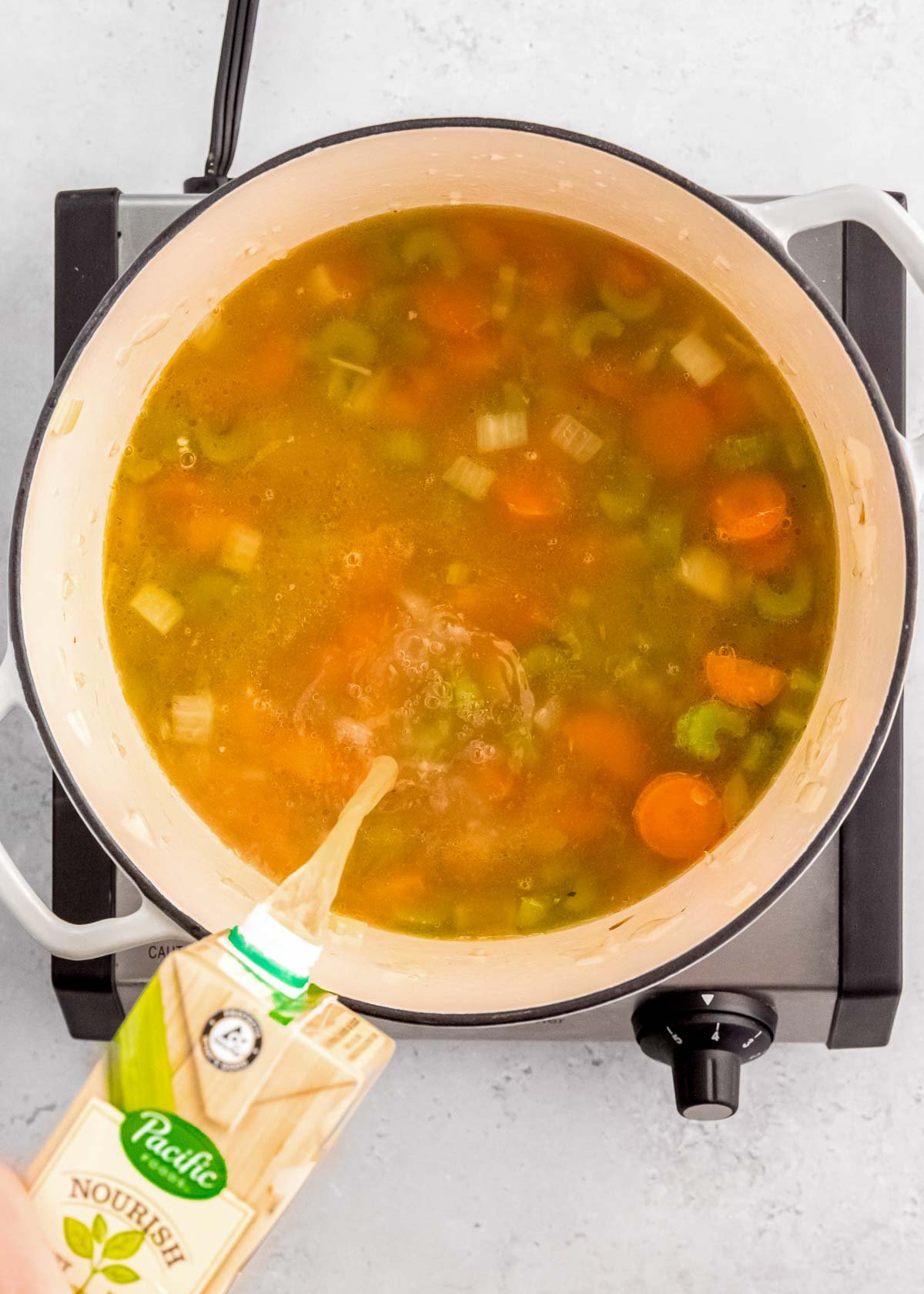 broth pouring into a dutch oven filled with simple vegetables