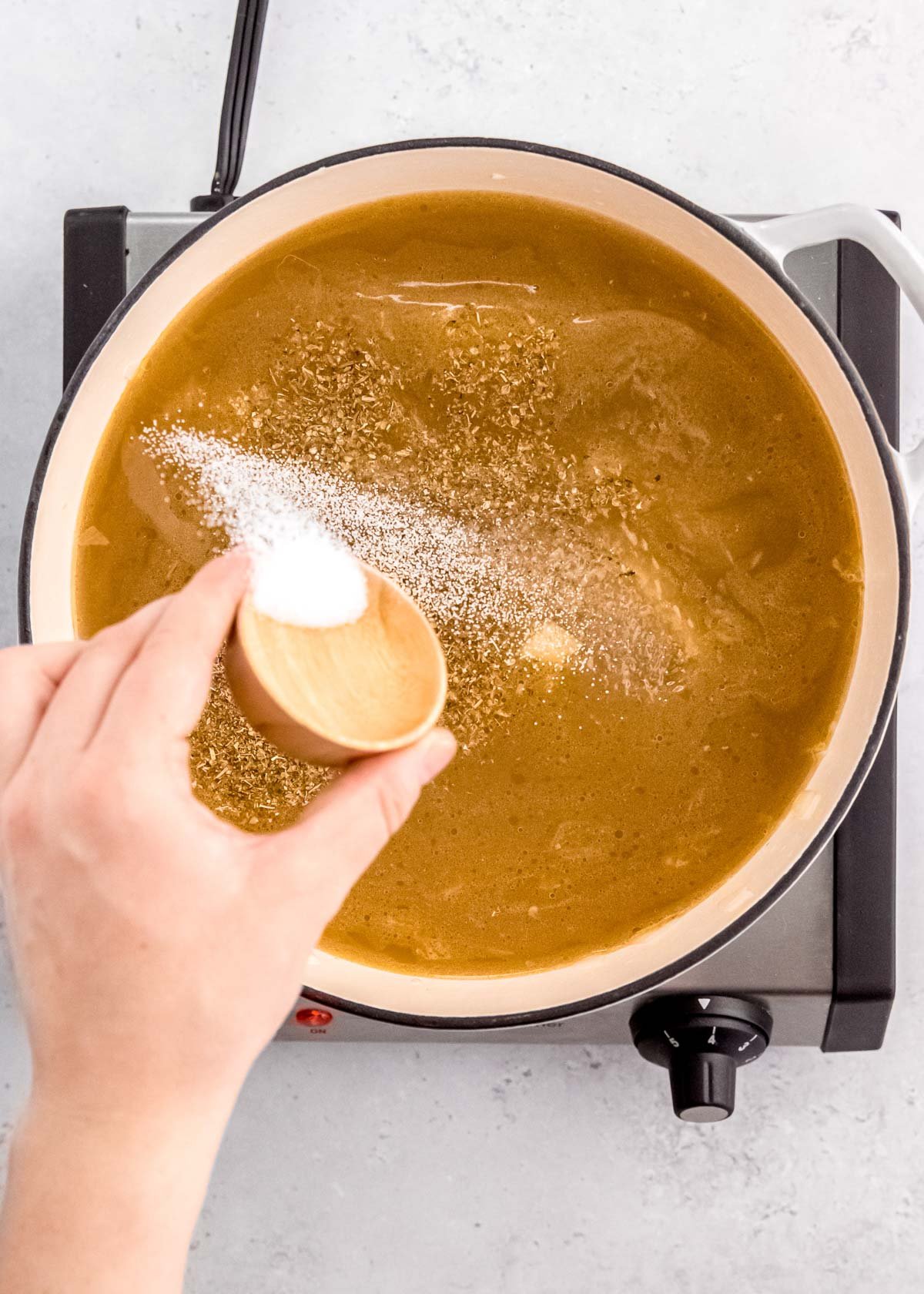 seasonings sprinkled into a dutch oven filled with broth and vegetables