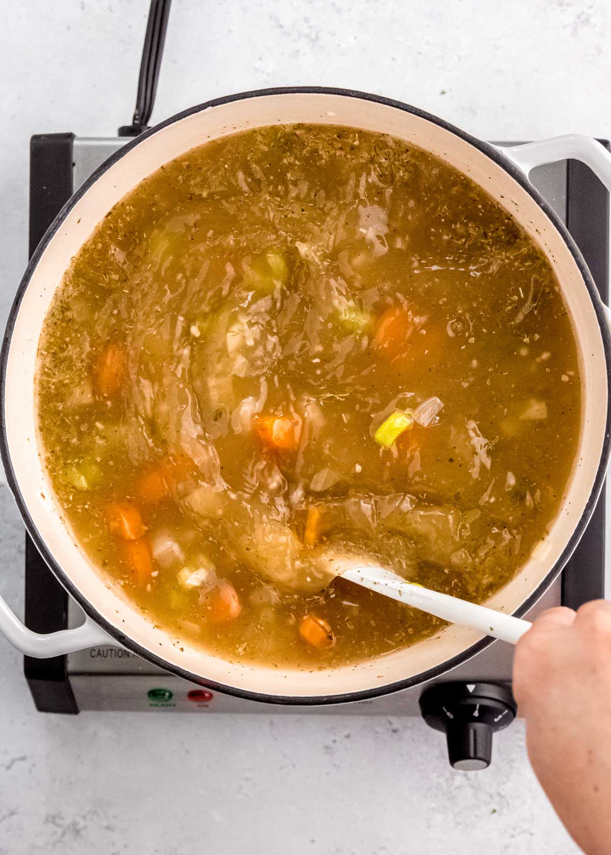 a large spoon stirring a pot full of simple veggies and seasonings in broth