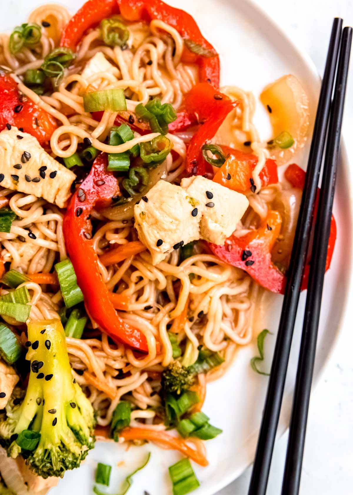 a white plate filled with stir fry with shirataki noodles, red peppers, broccoli, carrots, and onions; chopsticks on the side