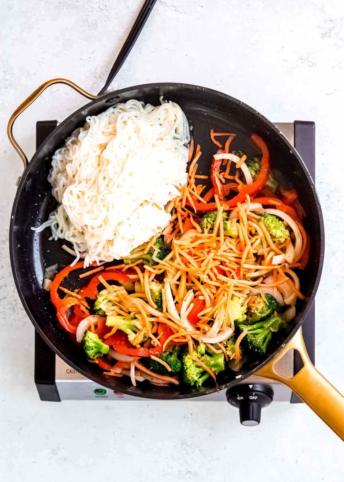 shirataki noodles and shredded carrots in a skillet with sauteed red peppers, onions, and broccoli