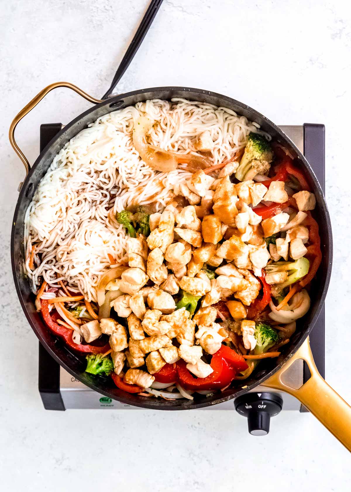 chicken, red peppers, onions, broccoli, carrots, and noodles in a large skillet
