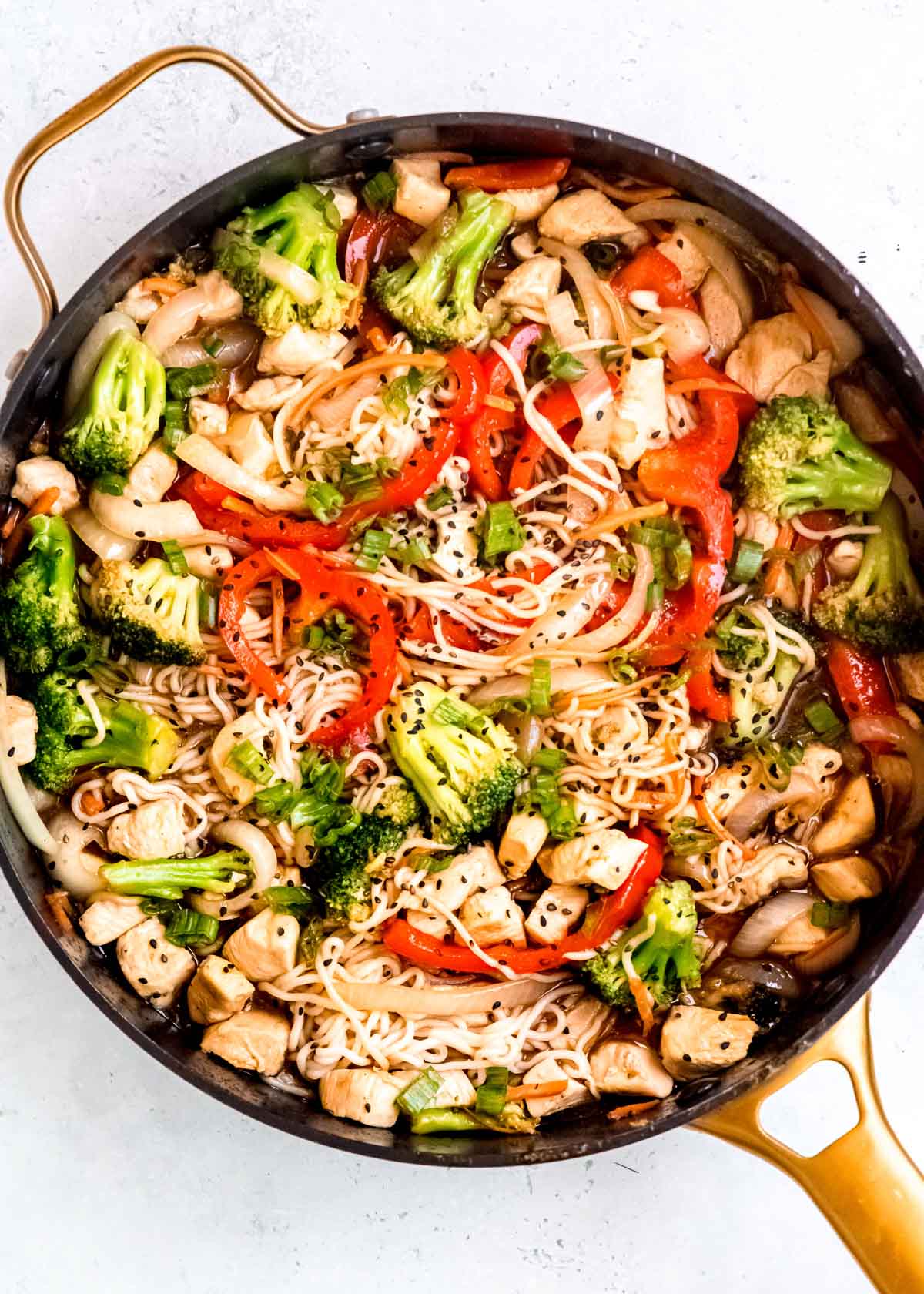 an overhead shot of a large skillet filled with shirataki chicken stir fry garnished with green onions and sesame seeds