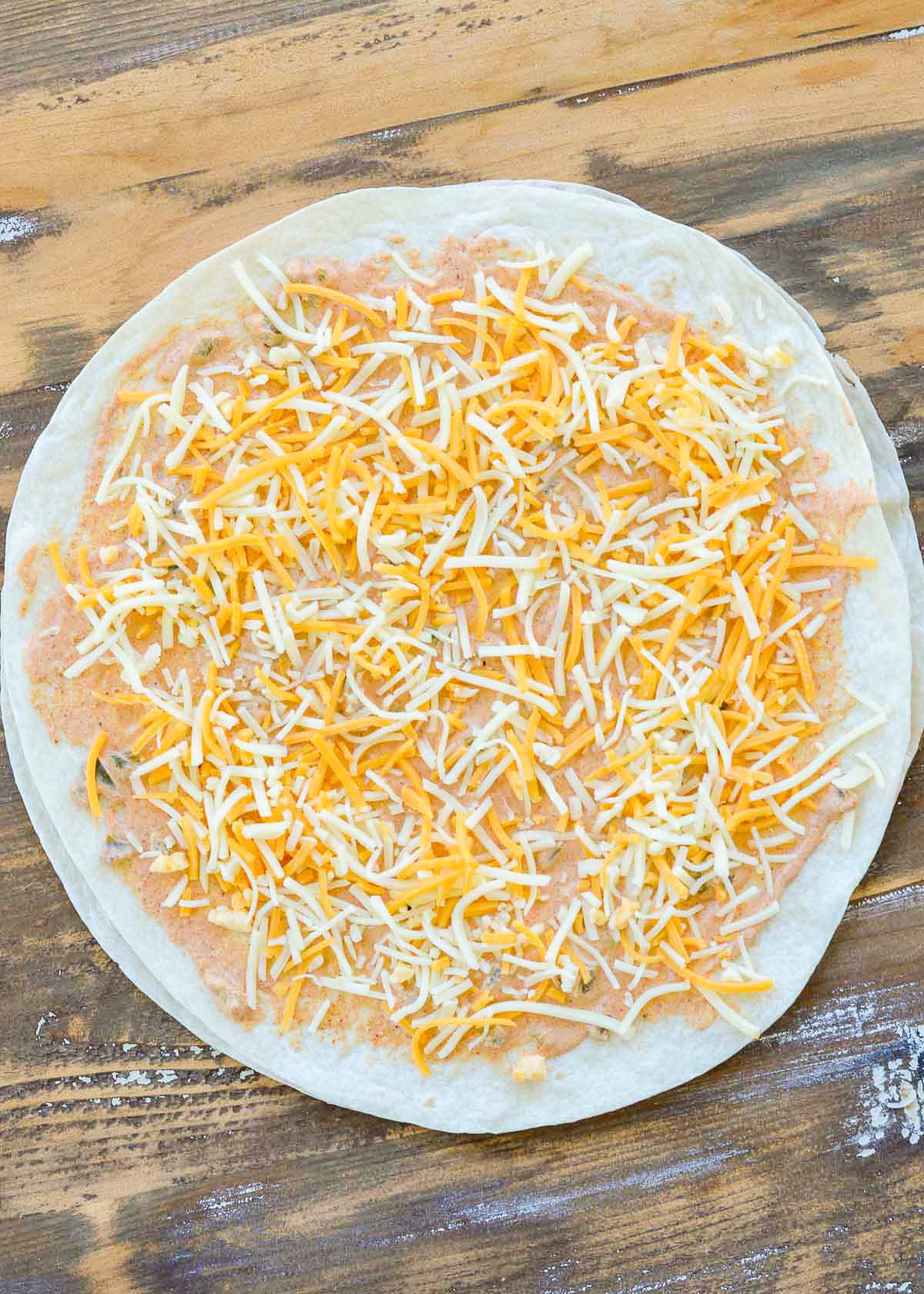 shredded cheese covering jalapeno sauce on a tortilla