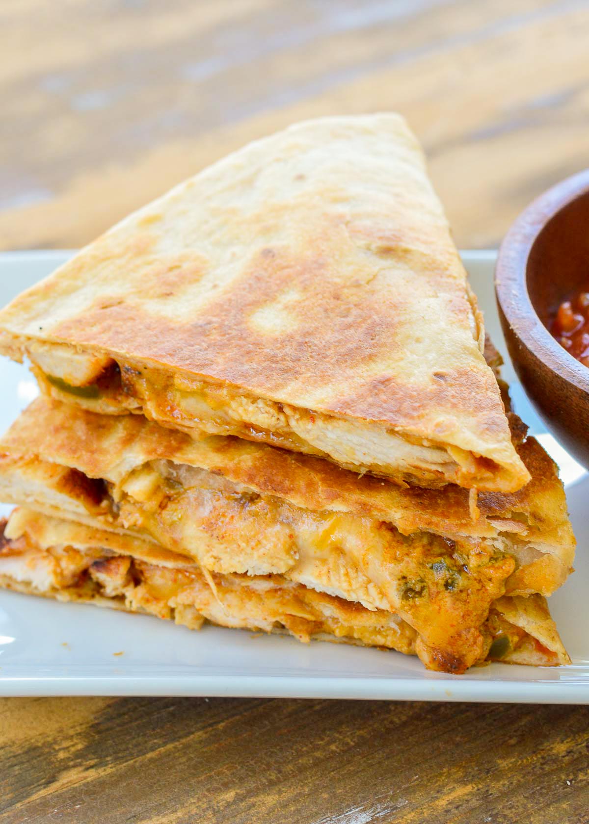 a toasty quesadilla cut into thirds and stacked on a white plate with a side of salsa