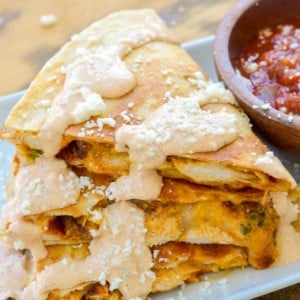 a cheesy chicken quesadilla cut into thirds and stacked on a white plate with a side of salsa; jalapeno cream sauce on top for the perfect taco bell chicken quesadilla copycat