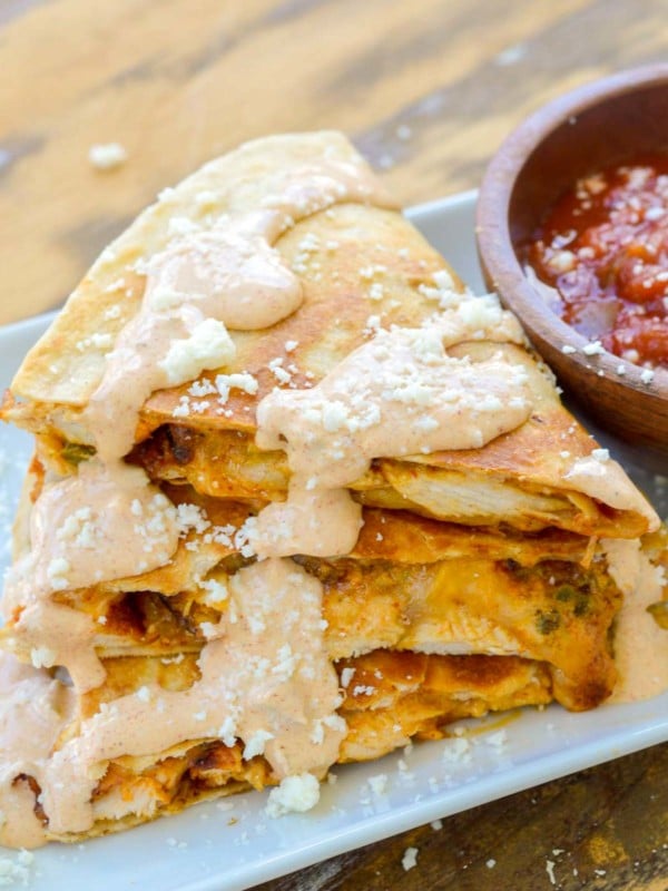 a cheesy chicken quesadilla cut into thirds and stacked on a white plate with a side of salsa; jalapeno cream sauce on top for the perfect taco bell chicken quesadilla copycat