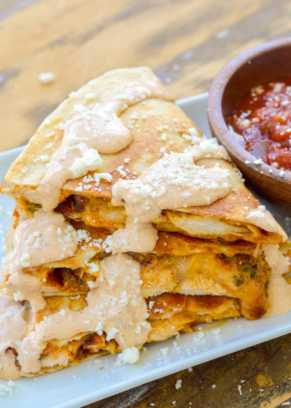 a cheesy chicken quesadilla cut into thirds and stacked on a white plate with a side of salsa; jalapeno cream sauce on top for the perfect taco bell chicken quesadilla copycat