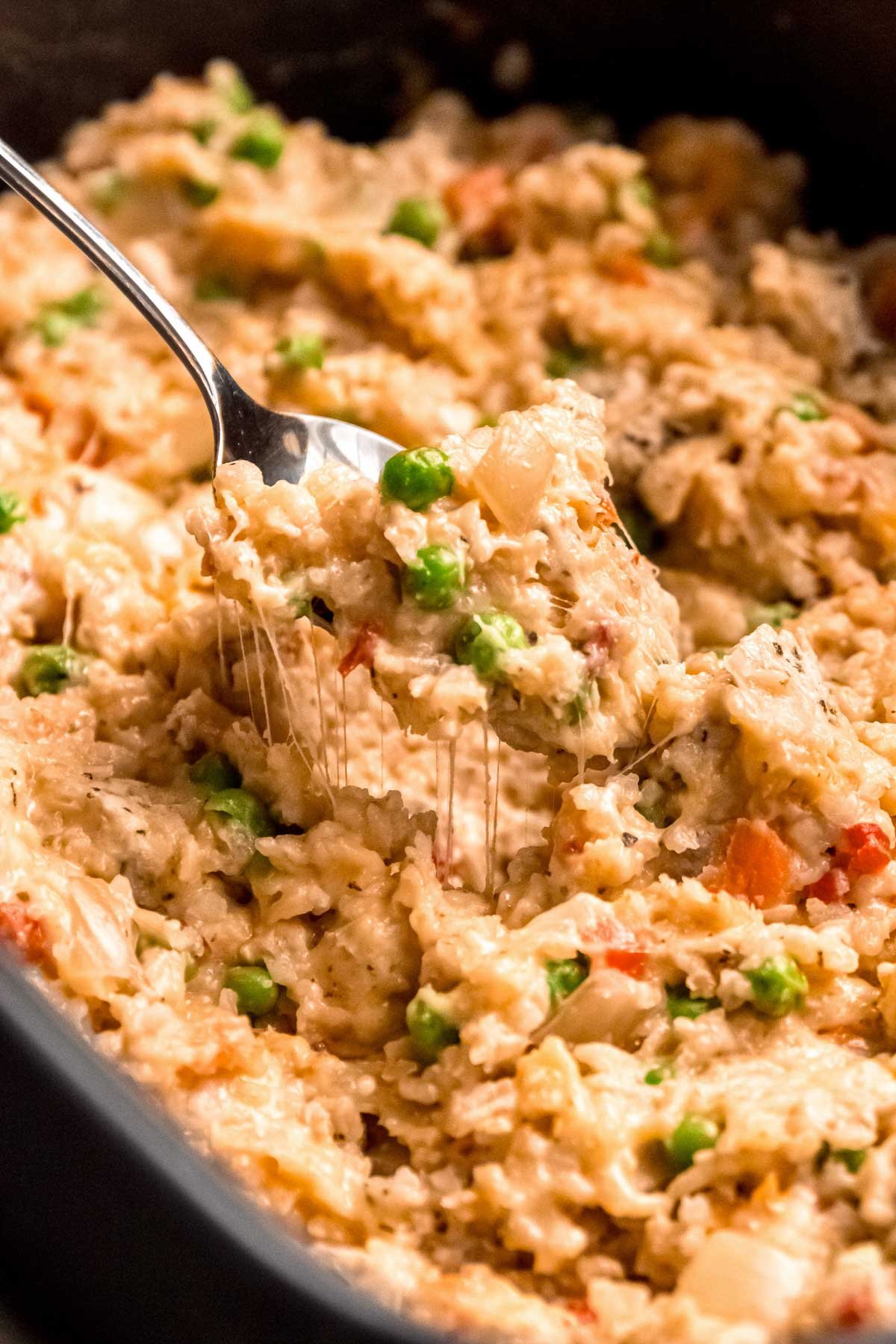 a big crockpot full of chicken, rice, peas, and carrots with gooey, melted cheese