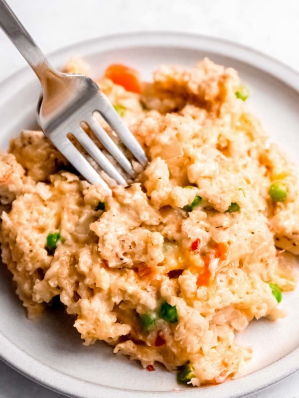 a fork in a big serving of chicken and rice with carrots and peas on a white plate